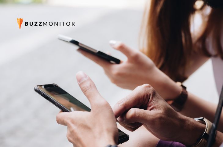 Duas pessoas usam smartphones lado a lado ao ar livre, representando o consumo de redes sociais.