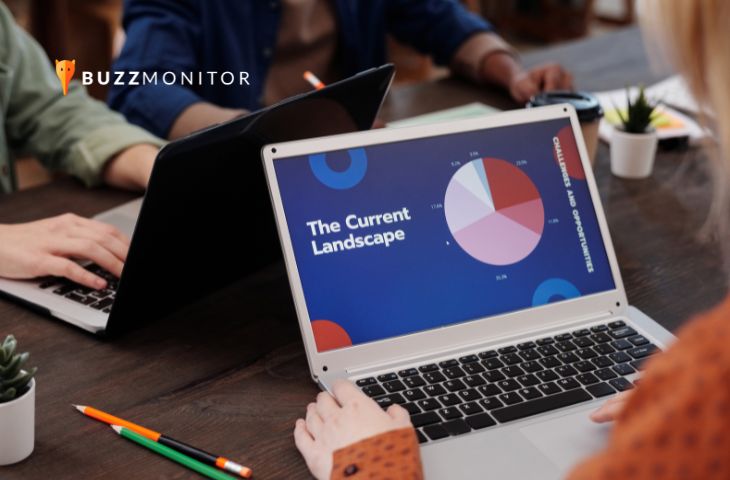 Pessoas reunidas à mesa de trabalho, com notebook exibindo slide de apresentação com gráfico de pizza sobre panorama de mercado