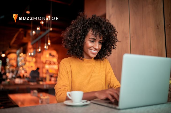 Mulher sorridente digita no notebook em ambiente aconchegante, representando o atendimento digital ágil.