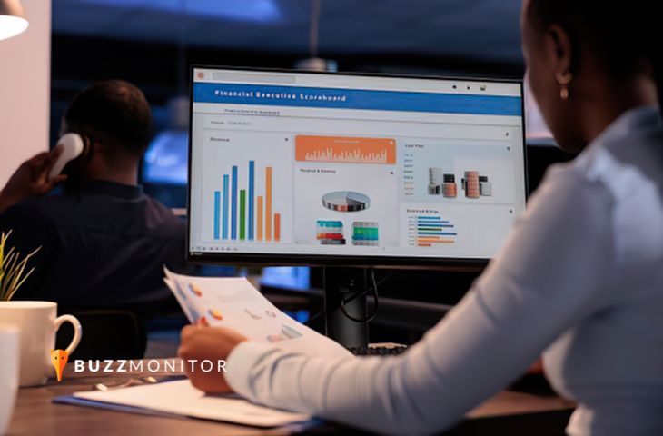 Mulher analisa dashboard executivo com gráficos na tela, segurando relatórios impressos para reportar à diretoria.