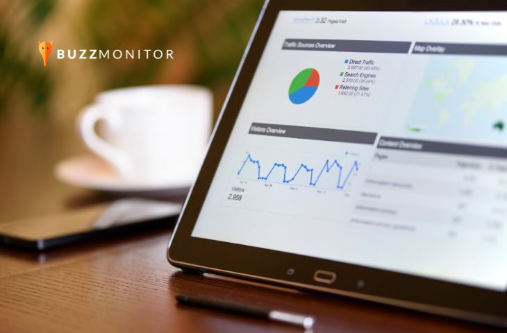 Tablet exibe dashboard de analytics com gráficos de tráfego e visitantes, sobre mesa de madeira.