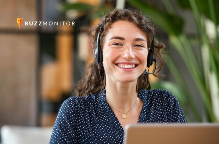 Mulher sorridente usando headset atende cliente em frente ao notebook, representando o time de CS.