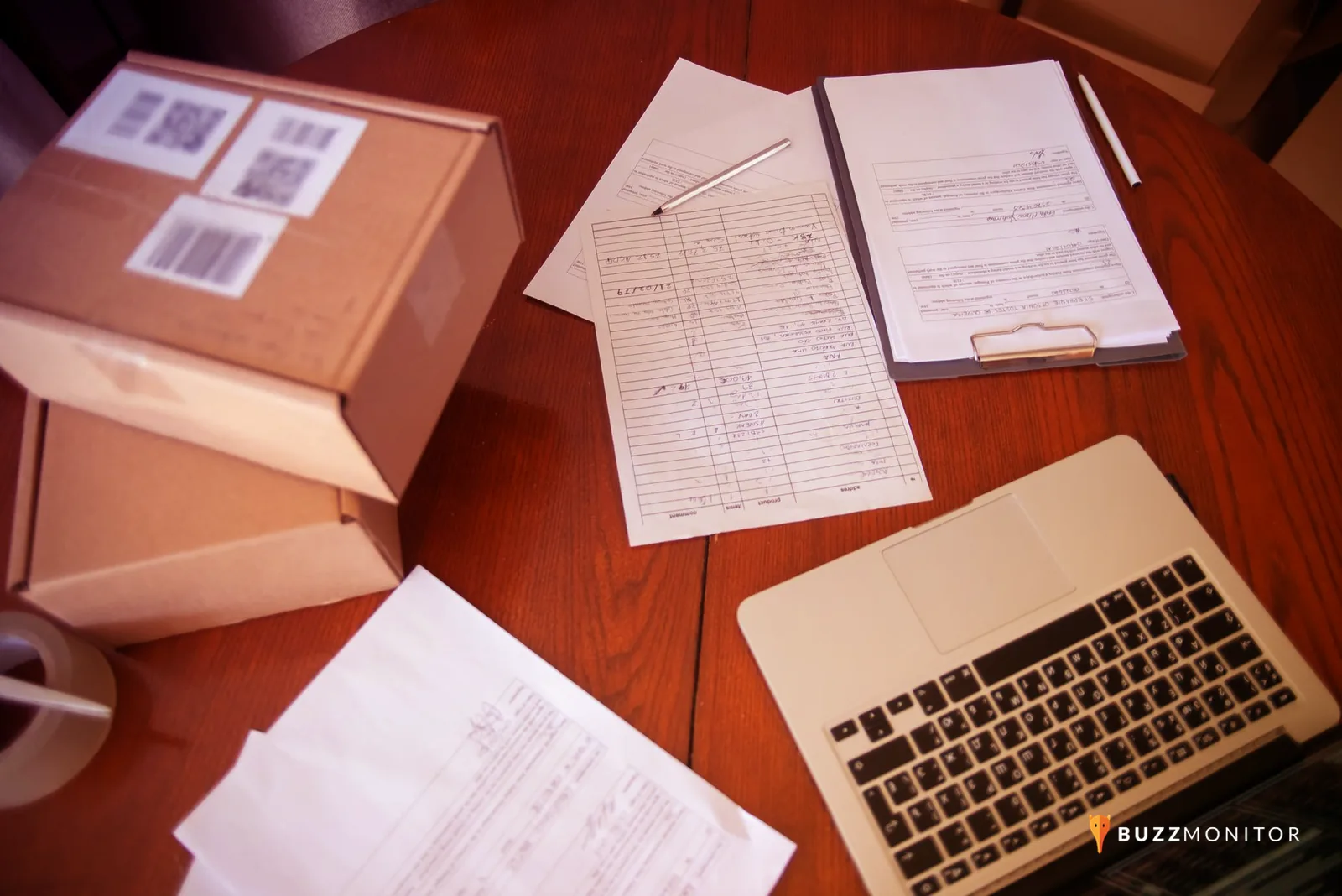 Atendente analisa informações de entrega em um notebook com caixas de encomenda sobre a mesa